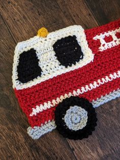 a crocheted red and white firetruck pot holder on a wooden floor