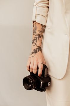 a person holding a camera in their right hand and wearing a white suit with tattoos on it