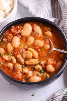 a bowl filled with beans and rice on top of a white cloth next to a spoon