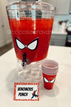 a drink dispenser sitting on top of a counter next to two cups