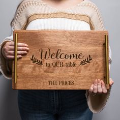 a woman holding a wooden sign that says welcome to our table the prices are $ 10