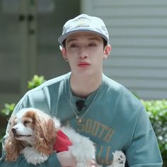 a young man holding a small dog in his lap while wearing a hat and sweater