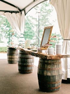 a wooden barrel table with plates and cups on it under a tented area that has white drapes