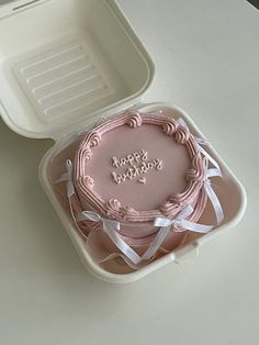 a pink cake in a plastic container with white ribbon around the edges that says happy birthday