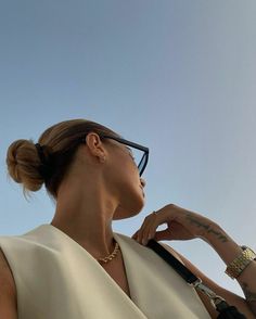 a woman wearing glasses and a white top looks up into the sky with her hand on her hip