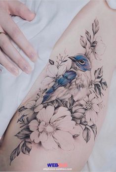 a woman's arm with flowers and a blue bird on it, while she is holding