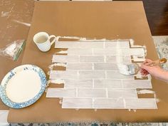 a person is painting a brick wall with white paint on the table next to a cup and saucer