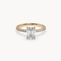 a gold engagement ring with an emerald cut diamond and pave set diamonds on the band