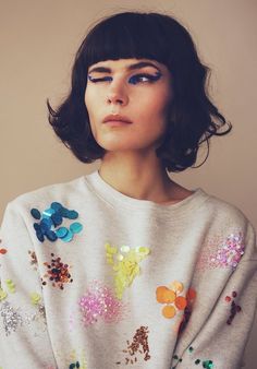 a woman with short black hair wearing a white sweater and colorful flowers on her shirt