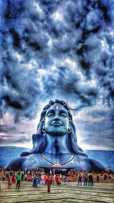 a large blue buddha statue sitting in the middle of a field under a cloudy sky