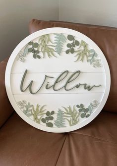 a white sign that says willow on it with green leaves and berries around the letters