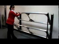 a woman in red shirt working on metal rail with black frame and white wall behind her