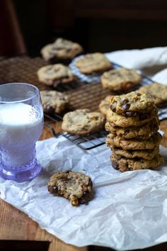 chocolate chip cookies and milk on a table next to a cooling rack with glass of milk