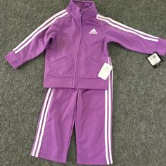 Purple Toddler Adidas Tracksuit Set. The Set Features A Full Zip Front Raglan Jacket With Dazzle Applied Stripes, Princess Seams, And Scoop Pockets. Embroidered Adidas Brand Mark On Left Chest And On The Back Of The Jacket. Elastic Waist Pant With Dazzle Applied Stripes And Embroidered Adidas Brand Mark On Left Leg. Nwt 12 Months Adidas Long Sleeve Playwear Sets, Adidas Fitted Winter Sets, Adidas Fitted Long Sleeve Sets, Winter Adidas Fitted Sets, Adidas Fitted Playwear Sets, Adidas Fitted Sets For Playwear, Raglan Jacket, Toddler Adidas, Brand Mark