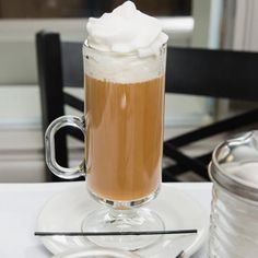 a cup of coffee with whipped cream in it on a plate next to a jar of milk