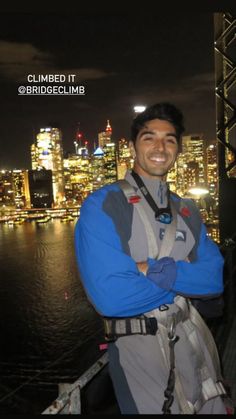 a man standing in front of a city at night with his arms crossed and smiling