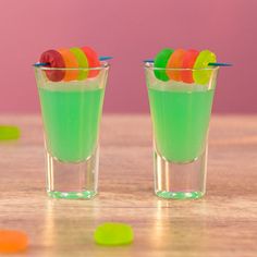 two shot glasses filled with jelly beans and gummy bears on top of a wooden table