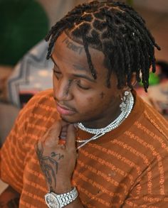 a man with dreadlocks is looking at his cell phone while wearing an orange shirt