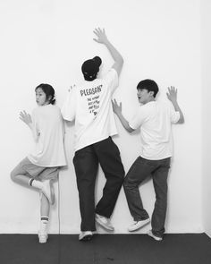 three young men standing next to each other in front of a wall with their hands up