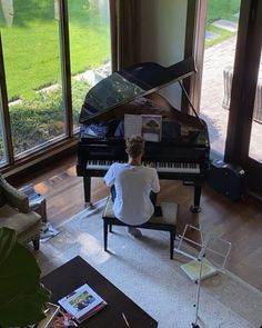 a woman sitting at a piano in front of a large open window with grass outside