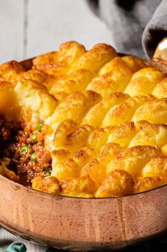 a casserole dish with meat and cheese in a wooden bowl on a table