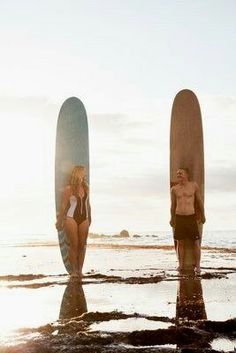 two people are standing on the beach with their surfboards