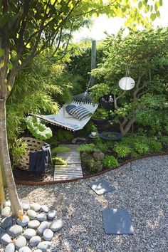 a garden with rocks, gravel and a hammock in the middle surrounded by trees