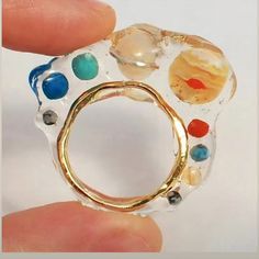 a hand holding a ring made out of glass with different colored stones on it's side