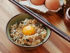 an egg sits on top of rice in a bowl with chopsticks next to it