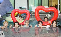 some people are posing in the water with large heart shaped balloons on their heads and hands