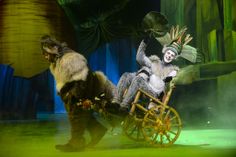 two people dressed as monkeys riding on a wooden cart in front of a green background