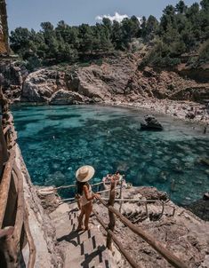 a woman in a straw hat is walking up some stairs to the water's edge