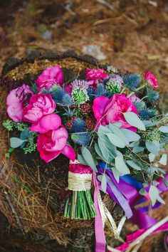 a bouquet of flowers sitting on top of a wooden basket next to a purple ribbon