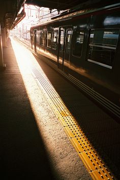 a subway train traveling down tracks next to a platform at night with the sun shining on it