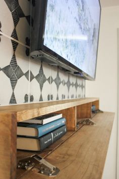 a flat screen tv mounted to the side of a wooden shelf with books on it