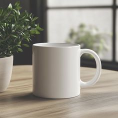 a white coffee mug sitting on top of a wooden table next to a potted plant