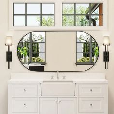 a bathroom with a large round mirror above the sink and two windows on the wall