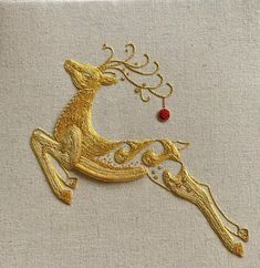 an embroidered gold deer ornament with a red bead on it's back