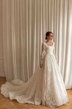 a woman in a white wedding dress standing on a wooden floor next to a curtain