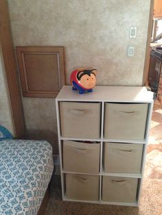 a bedroom with a bed, dresser and storage bins in front of the wall