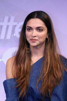 a woman with long brown hair wearing a blue top and posing in front of a white background