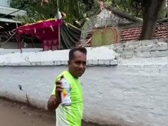 a man in green shirt holding up a can of soda next to a wall and trees