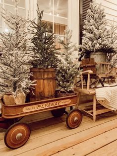 a wooden wagon with christmas trees in it sitting on a porch next to a window