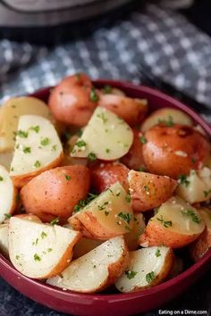 a red bowl filled with potatoes and parsley on top of a gray table cloth