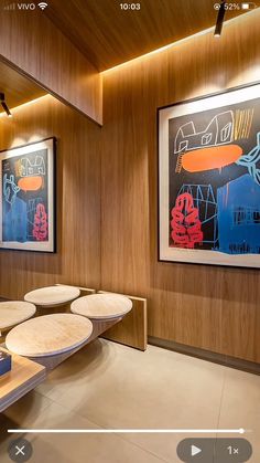 a room with wooden paneling and art on the wall, along with two round tables