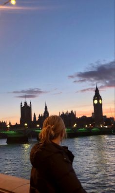 a woman sitting on a bench looking at the water and big ben in the background