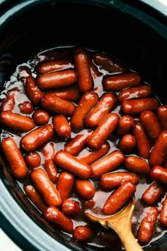 hot dogs are being cooked in the crock pot with a wooden spoon and is ready to be eaten