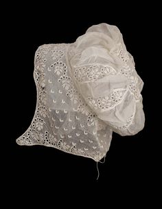 Woman’s embroidered mull cap with a puffed crown and chin pendants; embroidered in pattern of semicircular rows of eyelets around leafy sprigs with rows of small V-shaped motifs; embroidered circular piece at top of crown with gathered insertions of plain fabric between embroidered bands below; fine drawstring at nape of neck Regency Accessories, Historical Garments, Women's Caps, Regency Period, Period Dress, Historic Clothing, Baby Bonnets, Century Clothing