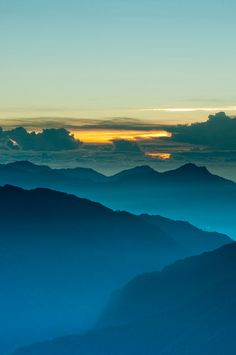 the sun is setting over some mountains in the foggy sky, as seen from an airplane