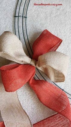 an orange and white bow is on the side of a wire wreath with red ribbon